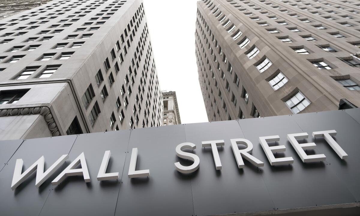 A view looking up at two tall buildings with a sign in the middle that says "Wall Street."