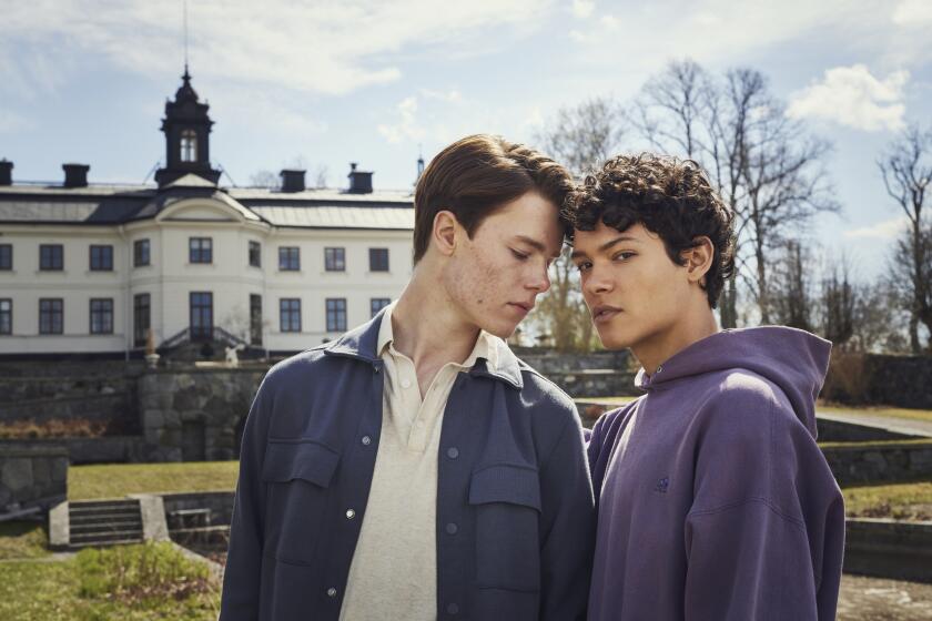 Two teenage boys share an intimate moment in the park outside a palace.