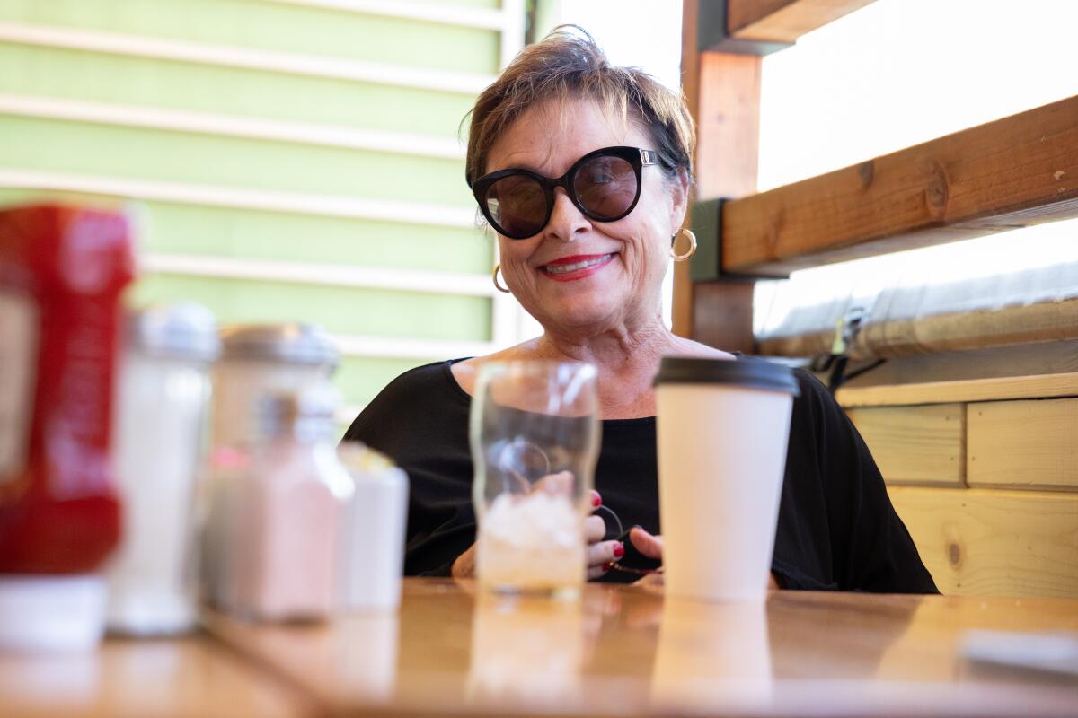 A woman in sunglasses sitting at a table, with condiments and drinks in the foreground