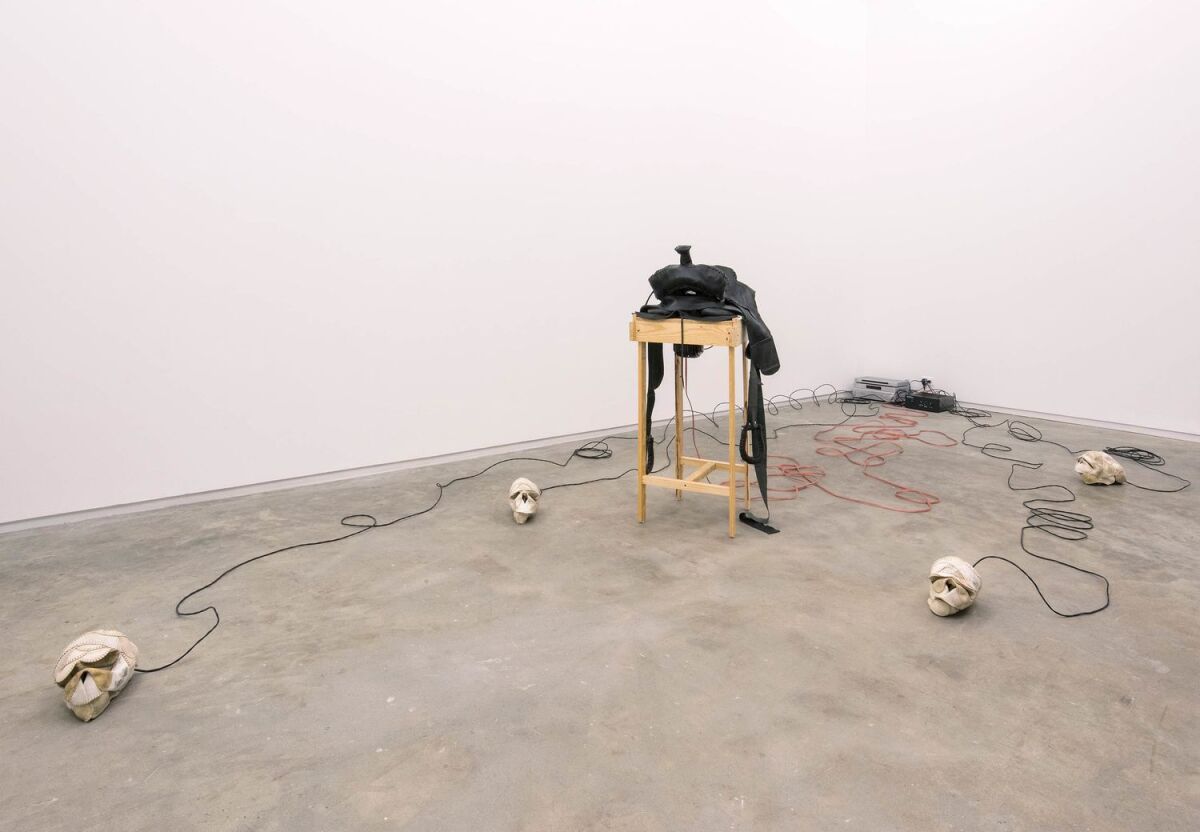 A gallery features skulls made from worn softballs connected by wires to a wooden plinth 