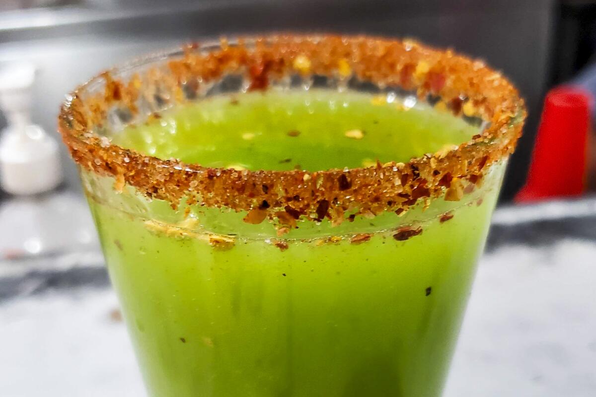 A green beverage in a glass with a red spice rim.