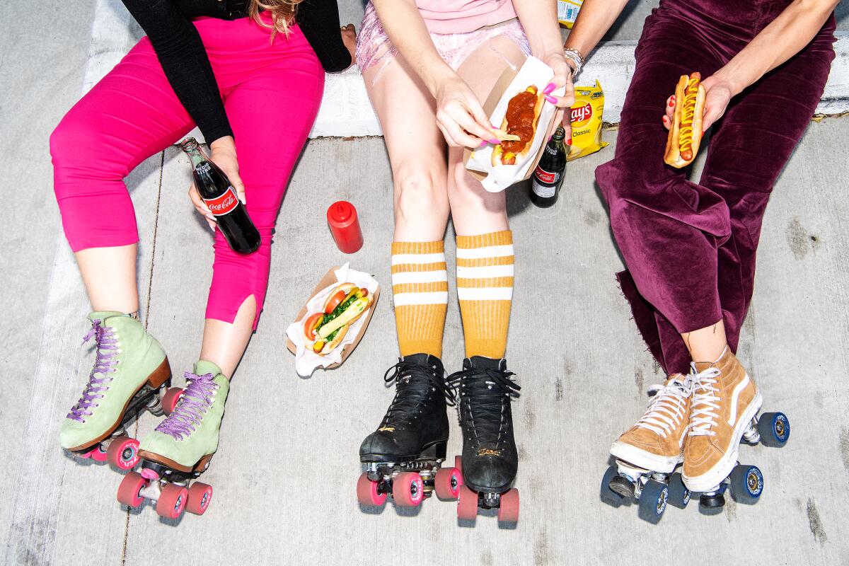 Three women in roller skates holding hot dogs and Cokes