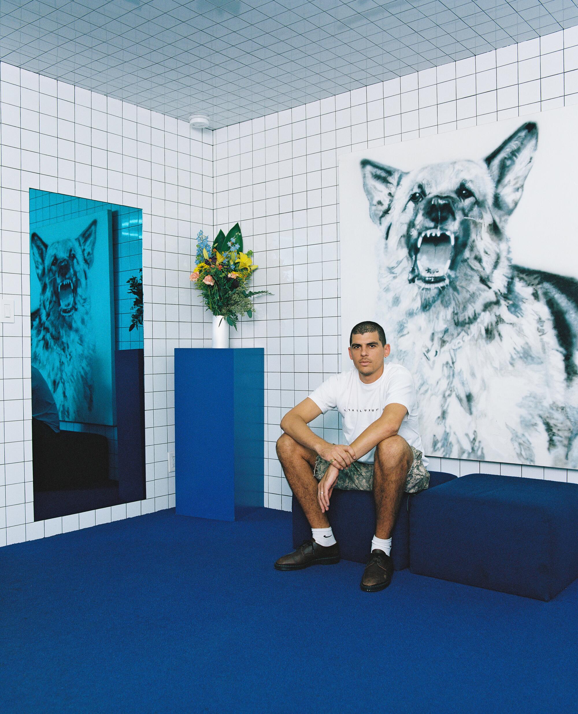 A man sits in front of a painting of a wolf. 