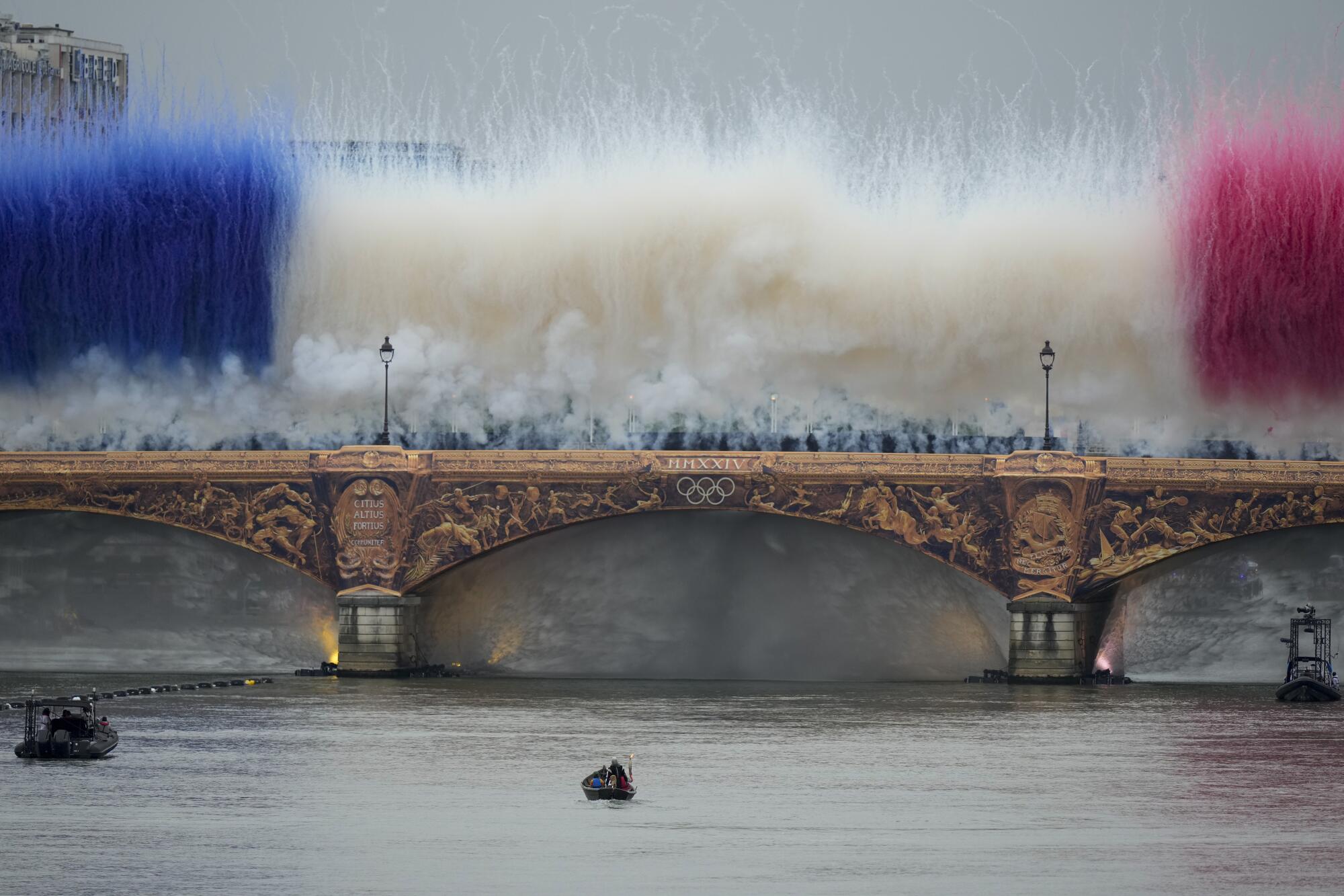 The Olympic torch travels by boat as ceremonial smoke in the colors of the France flag appear over the Seine River Paris.