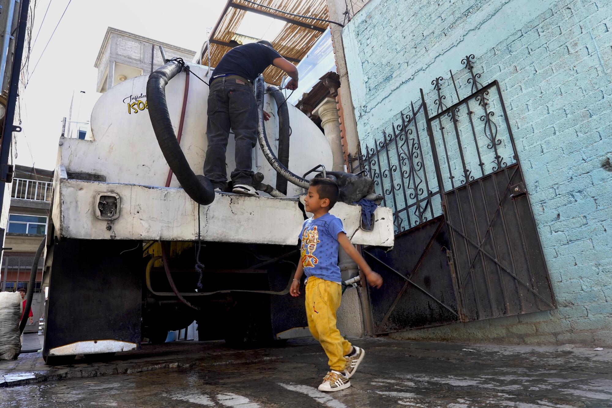 A man stands on a water tanker as a 5-year-old boy walks behind it.