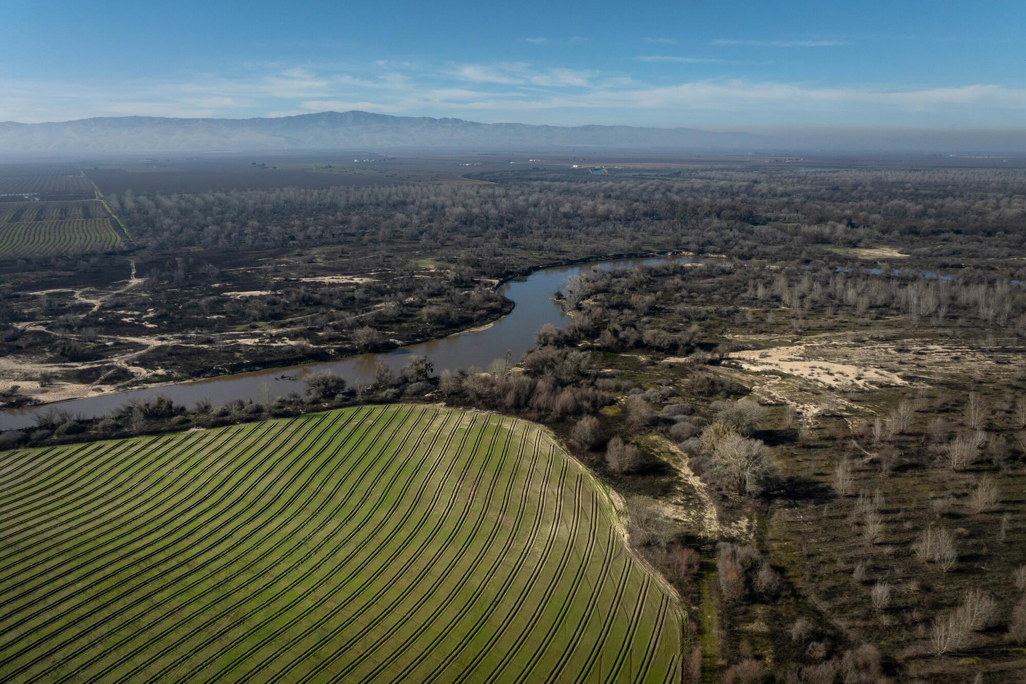 An aerial view of the San Joaquin River flowing past agricultural fields and forested land.