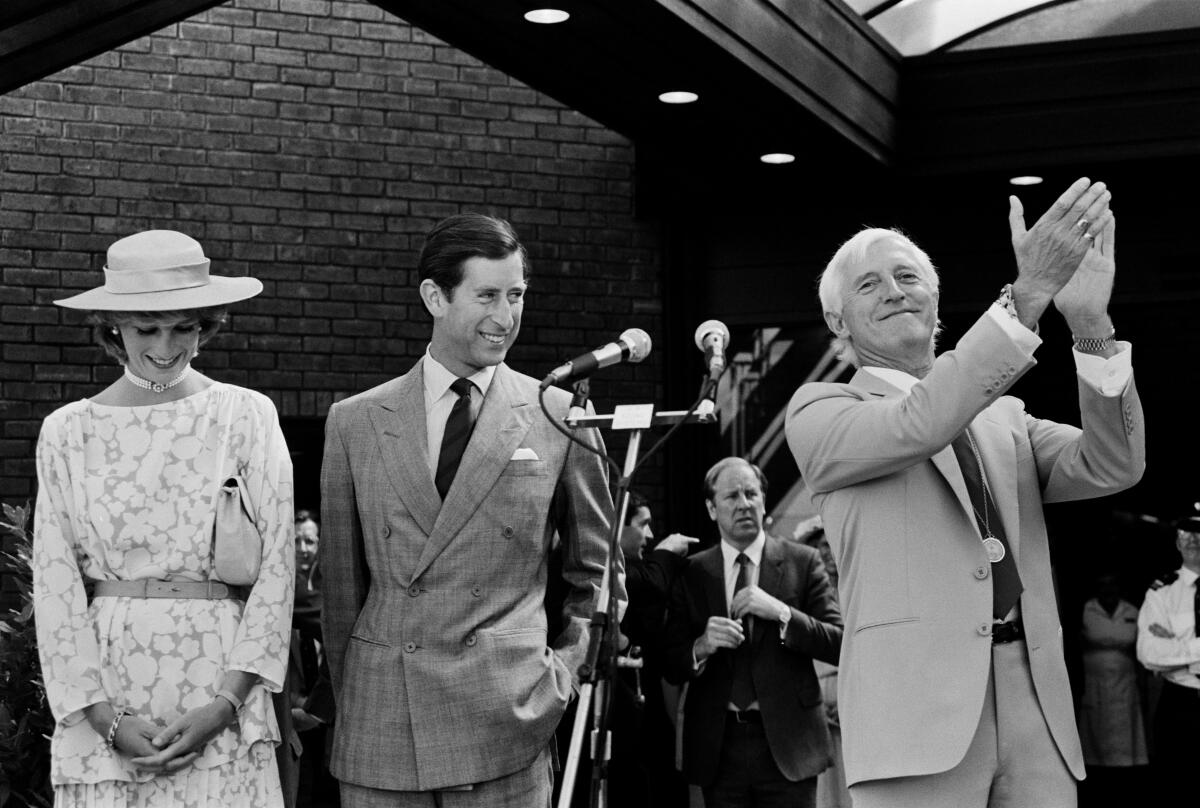 A man claps at a microphone next to Prince Charles and Princess Diana in a black-and-white photograph.