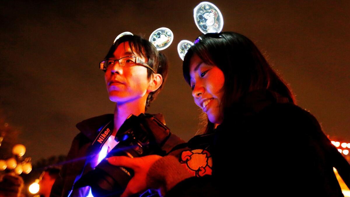 Shinya Yoshida, left, and Akiko Shiho, both of Tokyo, wear acrylic glow Mickey Mouse headbands to commemorate the return of the Main Street Electrical Parade.