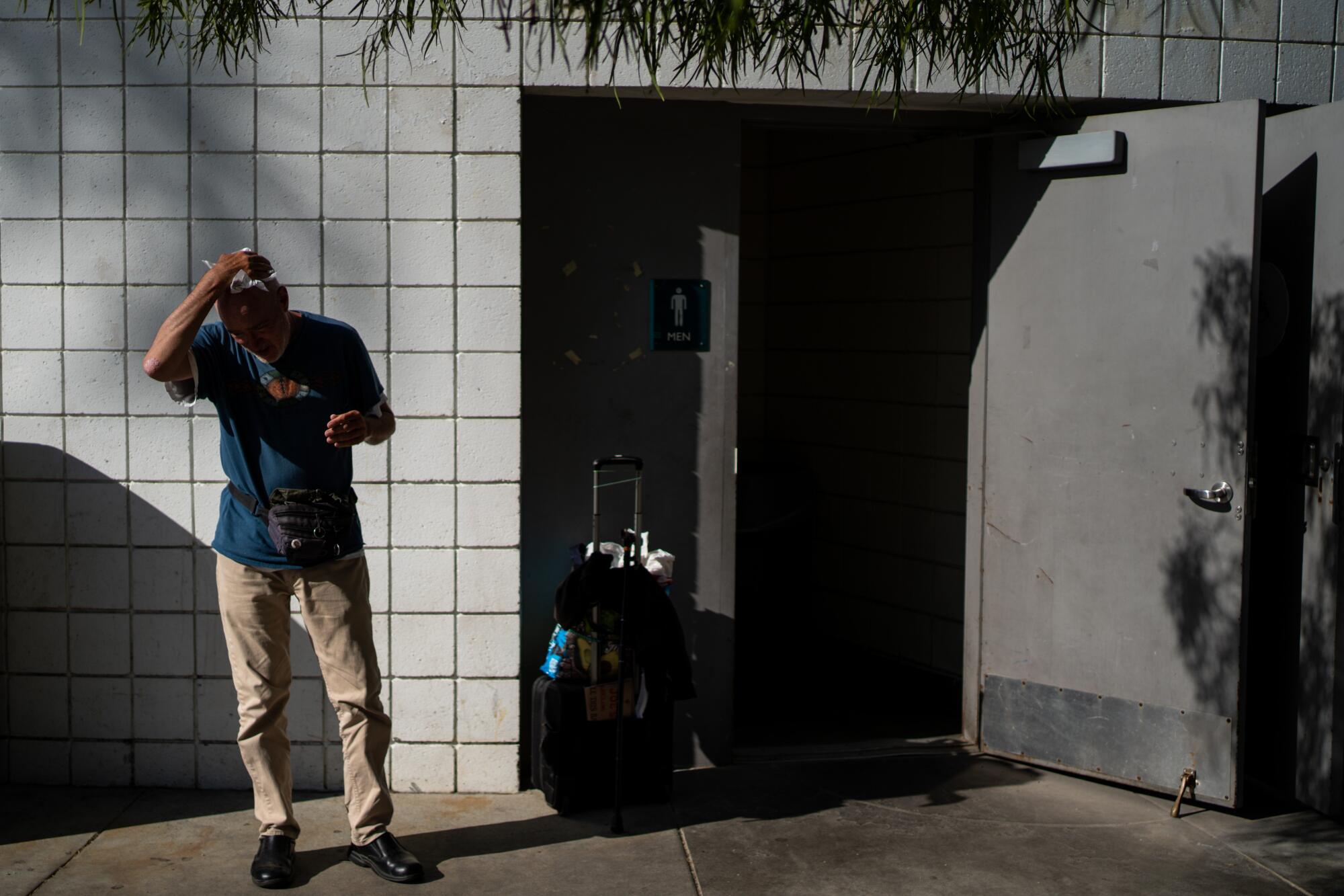 Terrance Whitten with a rolling suitcase outside a restroom.