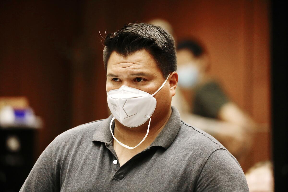 A man in a white mask and a polo shirt in a courtroom