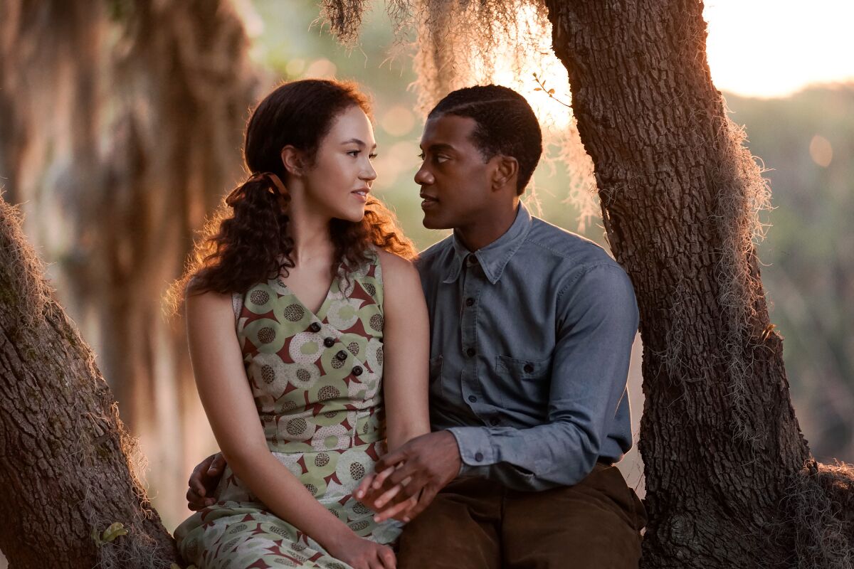 A young couple sits in the crook of a tree, gazing into each other's eyes.