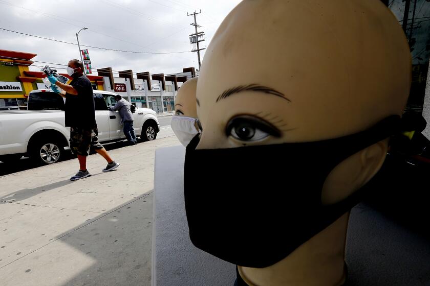 LOS ANGELES, CALIF. - APR. 2, 2020. A pair of vendors who declined to be identified sell face masks along San Pedro Street in the nearly deserted garment district of Los Angeles, where business has been largely suspended as a precaution against spreading the novel coronavirus. (Luis Sinco/Los Angeles Times)