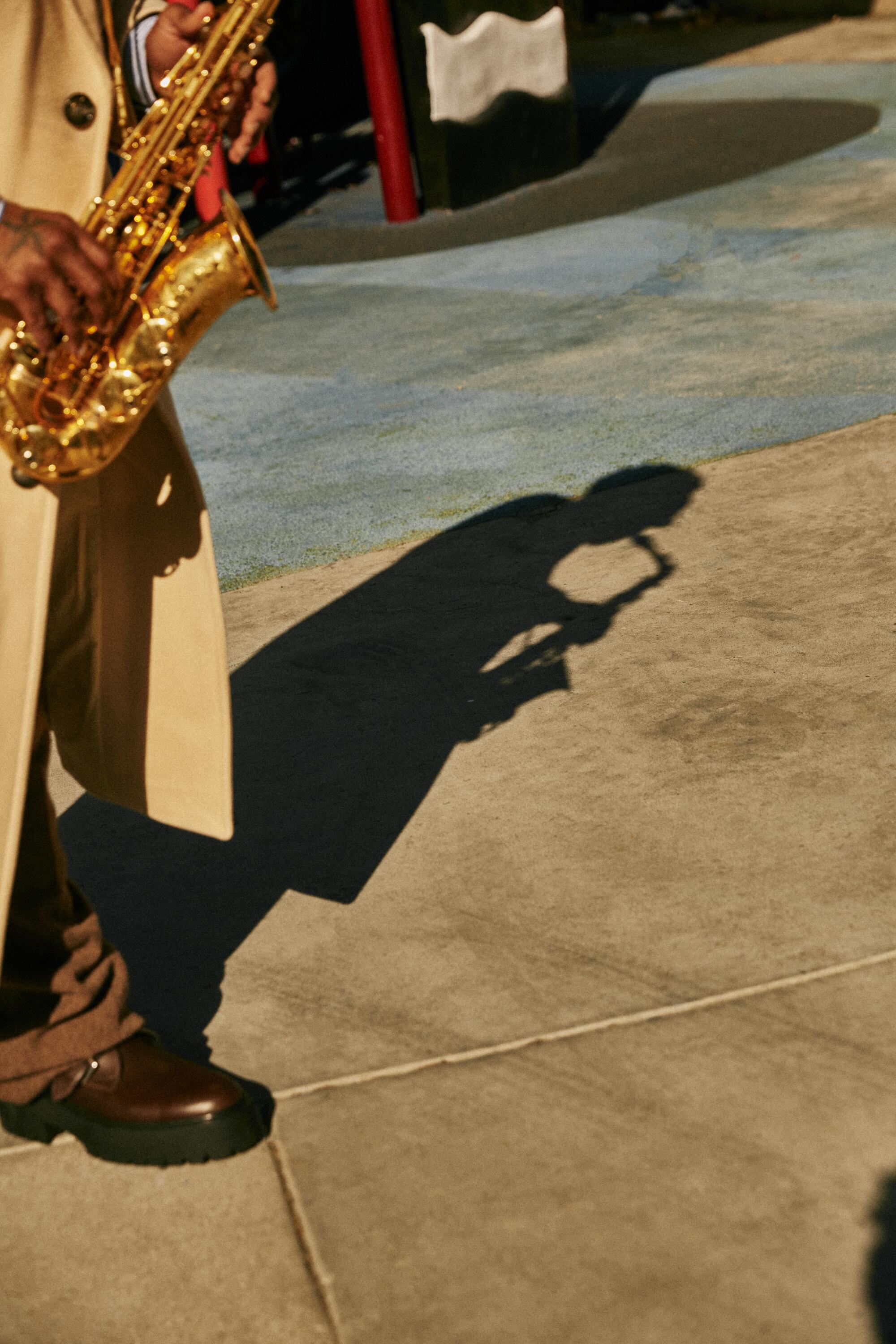Musician plays saxophone on the street, casting a shadow.