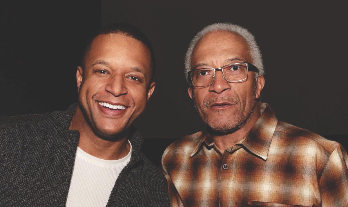 Two men, one in a jacket and another in a plaid shirt and glasses, pose for a portrait