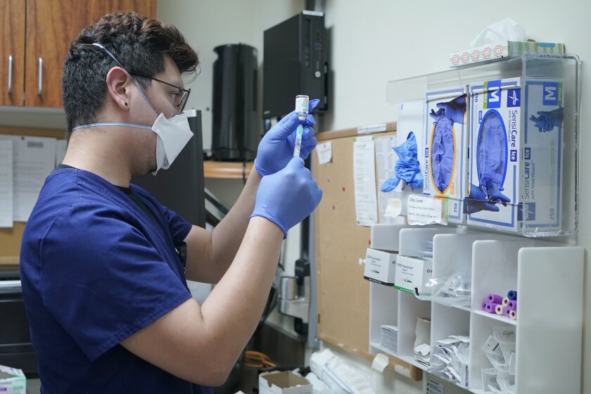 A person in mask and plastic gloves fills a syringe from a vial.