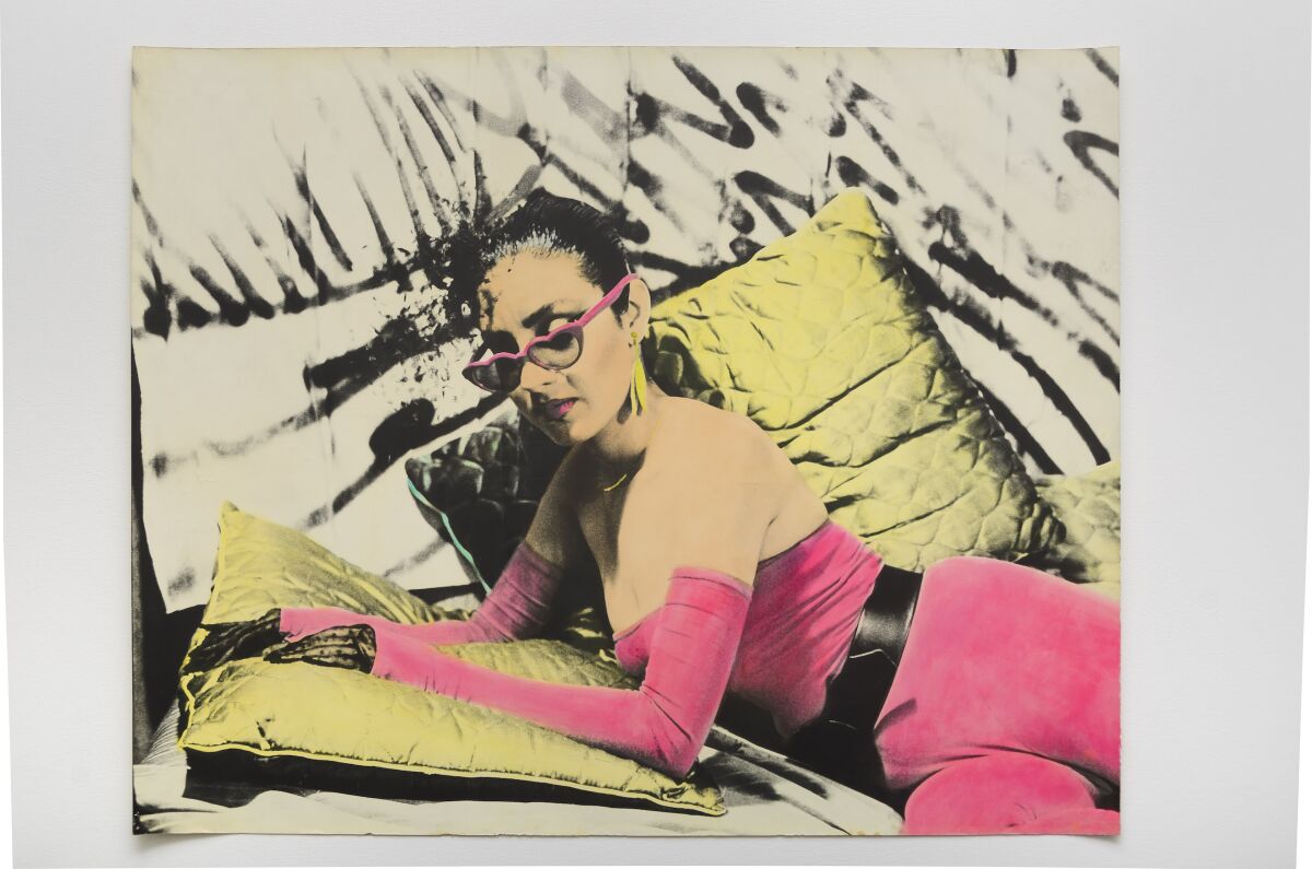 A black-and-white image shows a woman lying on a couch wearing sunglasses, her bodysuit painted a shade of bright pink.