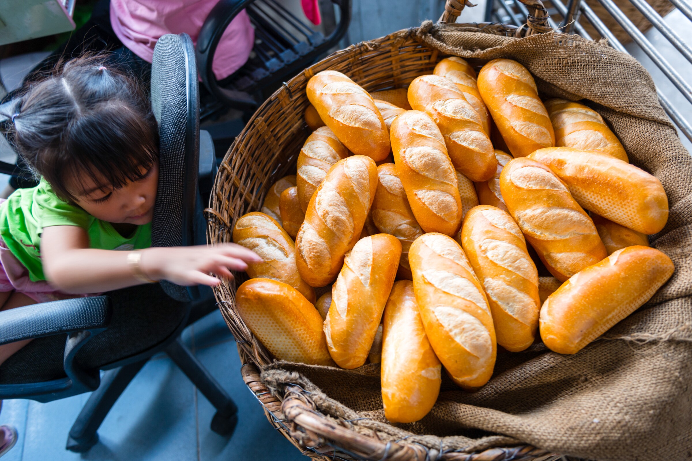 A little girl reaches for a basket of banh mi loaves in a bakery in Ho Chi Minh City, Vietnam.