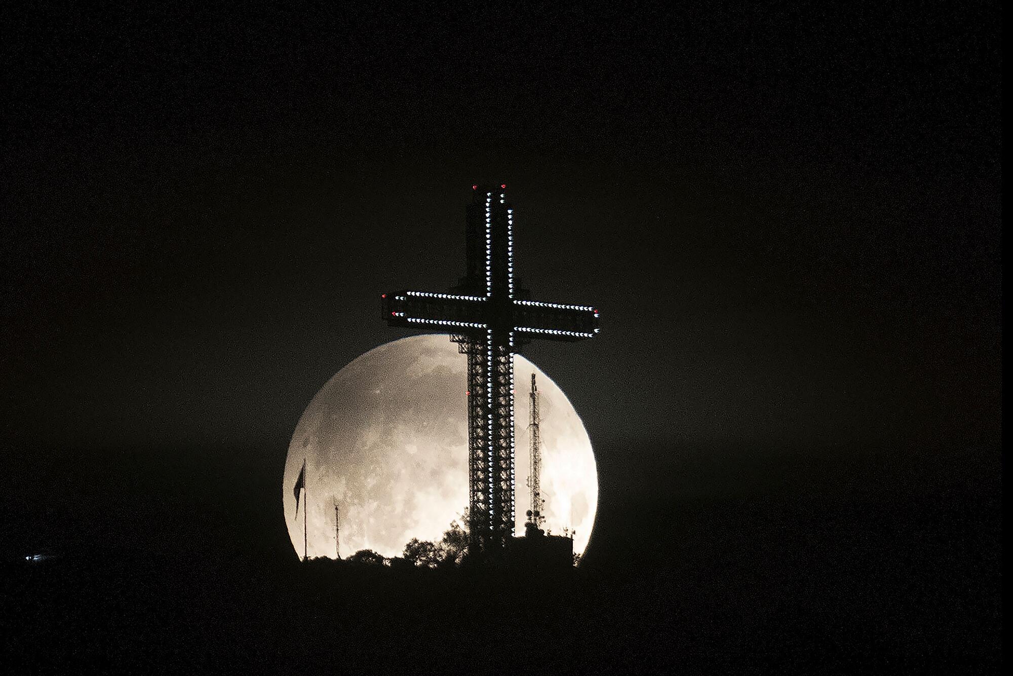 The full moon rises behind an illuminated cross.