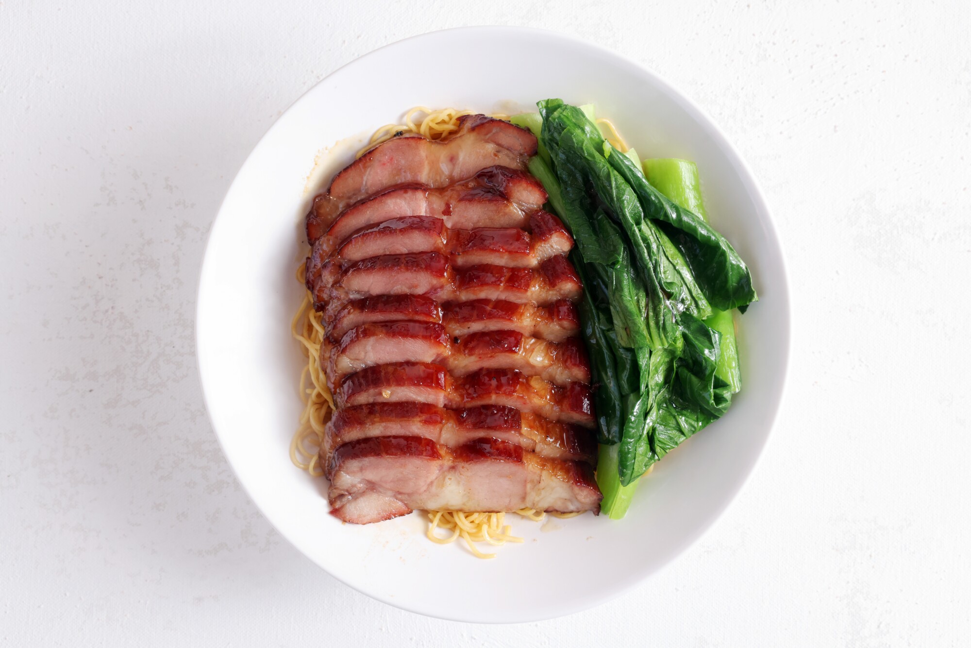 Pork and greens on a bed of noodles in a bowl with bok choy.