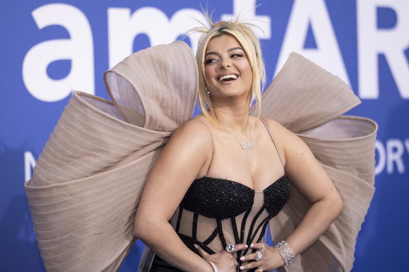Bebe Rexha holding her hands to her hips and posing for pictures in a black and beige mesh gown with a giant bow in the back