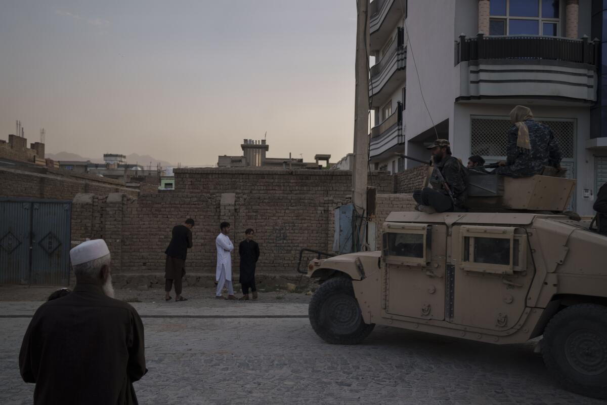 Afghans watch as Taliban fighters ride atop a Humvee in Kabul.