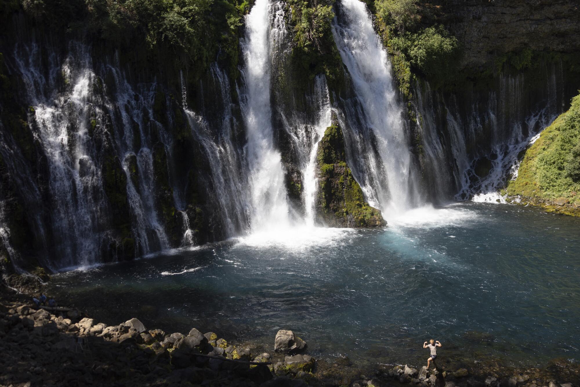 A visitant poses with arms raised connected a stone astatine Burney Falls.
