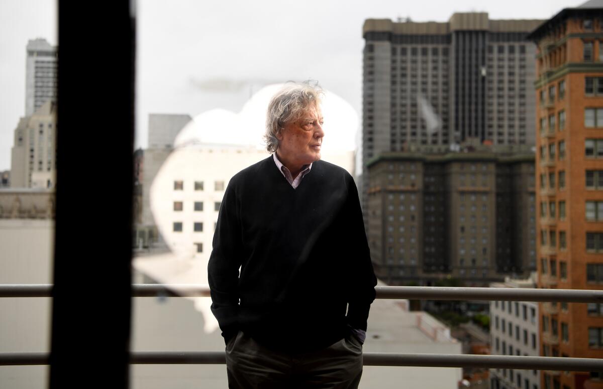 Tom Stoppard stands in front of a window looking out toward the San Francisco skyline.