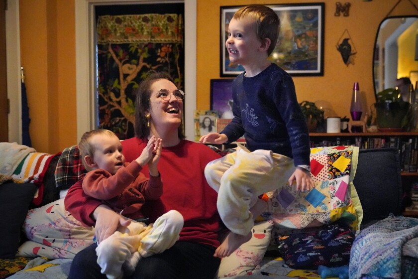Heather Cimellaro holds her three-year-old son Charlie while his twin brother, Milo, jumps on a couch at their home, Wednesday, Jan. 5, 2022, in Auburn, Maine. Heather Cimellaro is one many parents concerned about the omicron surge and the dilemma it's posing for families of children too young to be vaccinated. (AP Photo/Robert F. Bukaty)