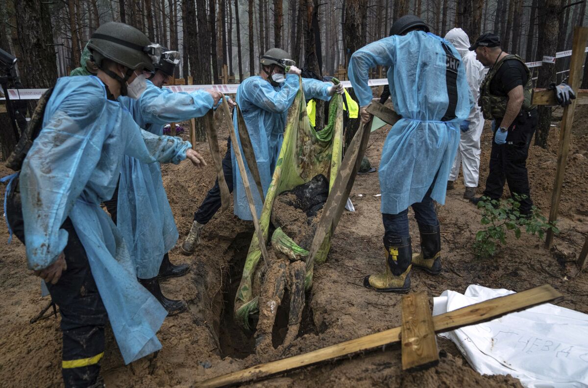 عمال يرفعون جثة مغطاة بالتراب من حفرة في الأرض.