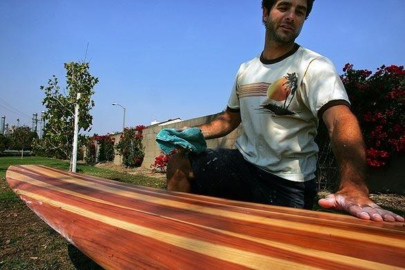 The Long Beach neighborhood of Island Village is considering a change of counties to become part of Seal Beach in Orange County. Sitting on a grassy walkway, Bradley DiMario polishes an 8-foot redwood surfboard he is making in Island Village.