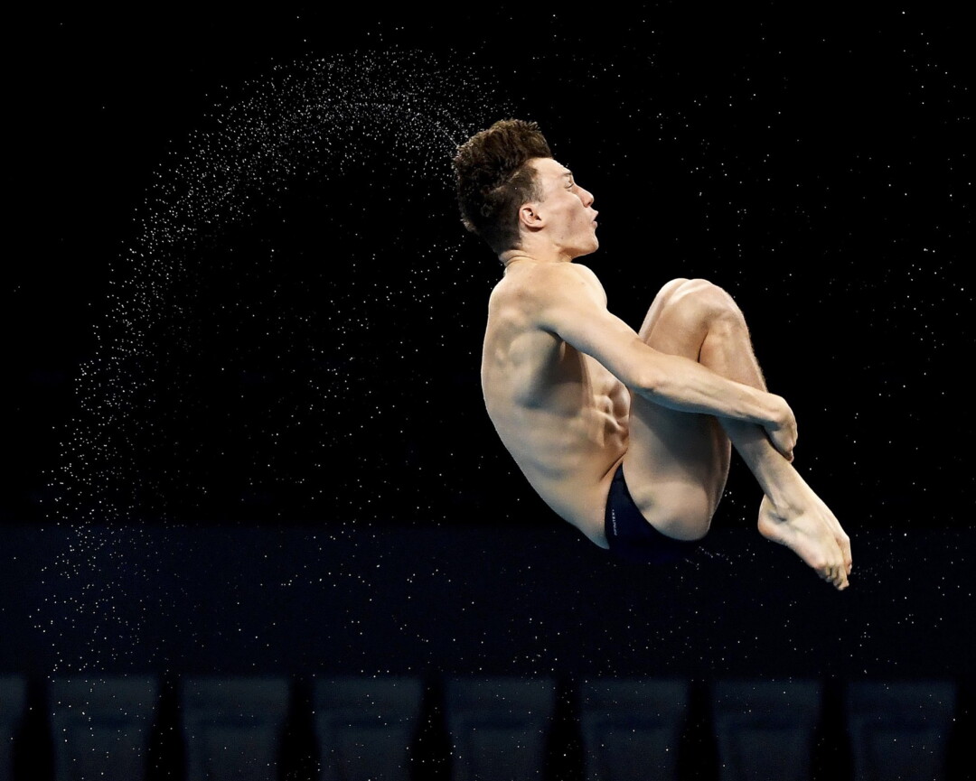 A diver holds his legs in midair.