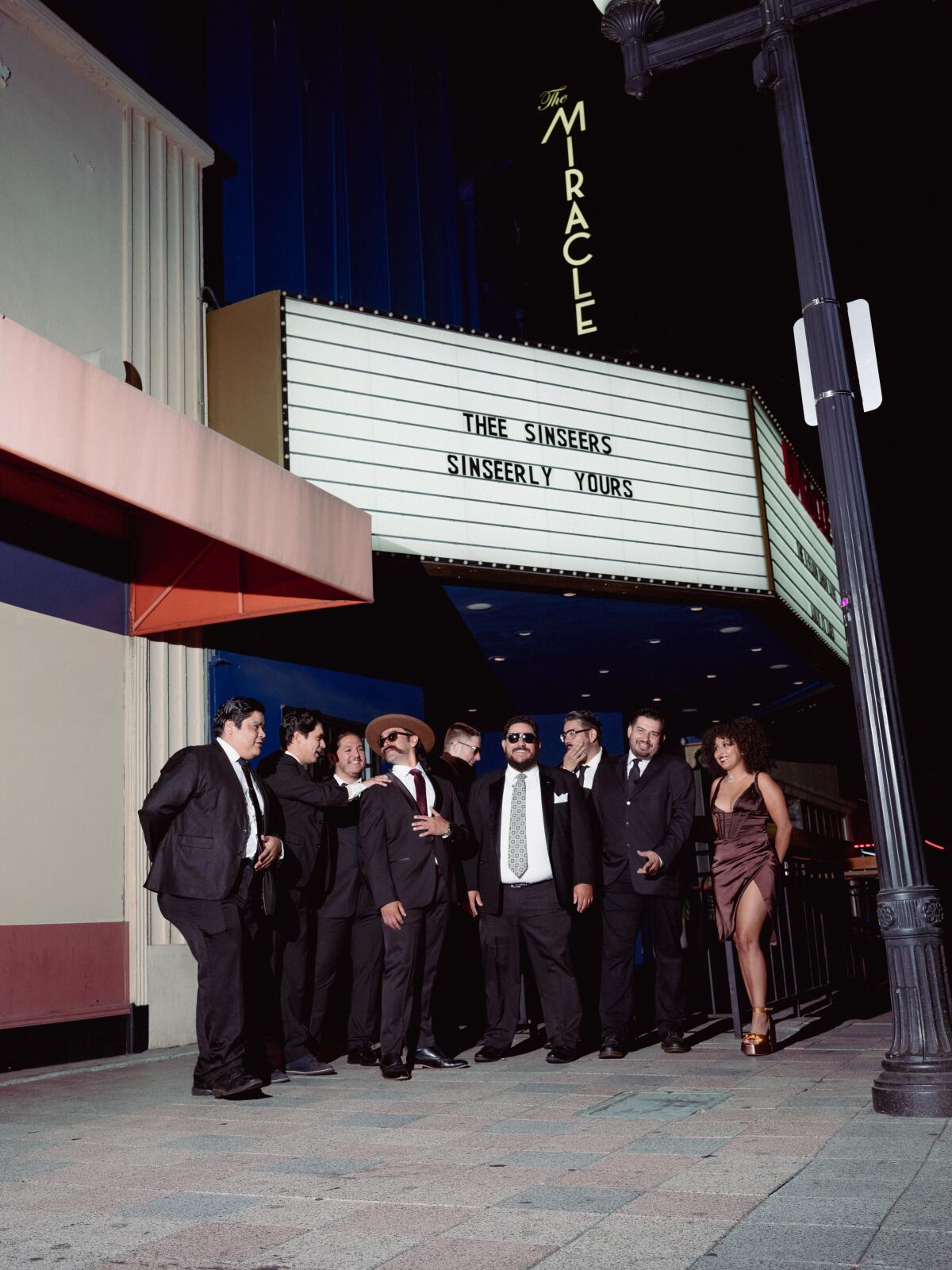 A group of people stands on a sidewalk outside a theater