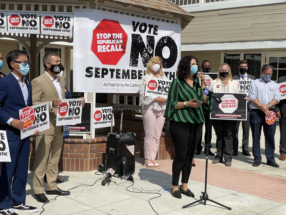 An outdoor news conference with signs that say Stop the Republican Recall, Vote No September 14th