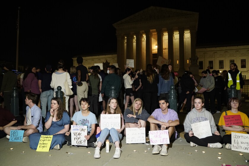 People sit outside the Supreme Court with signs reading "Pro Choice" and "Abortions Are Pro-Life."