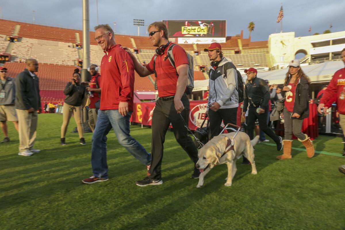 USC long snapper Jake Olson walks on a football field with the aid of his service dog, Quebec, in 2018