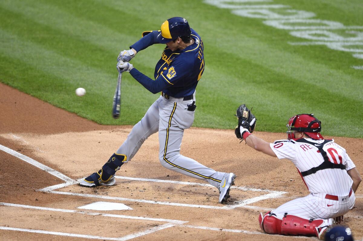 Milwaukee Brewers' Christian Yelich, left, hits a single during the first inning of a baseball game in front of Philadelphia Phillies' J.T. Realmuto (10), Monday, May 3, 2021, in Philadelphia. (AP Photo/Derik Hamilton)