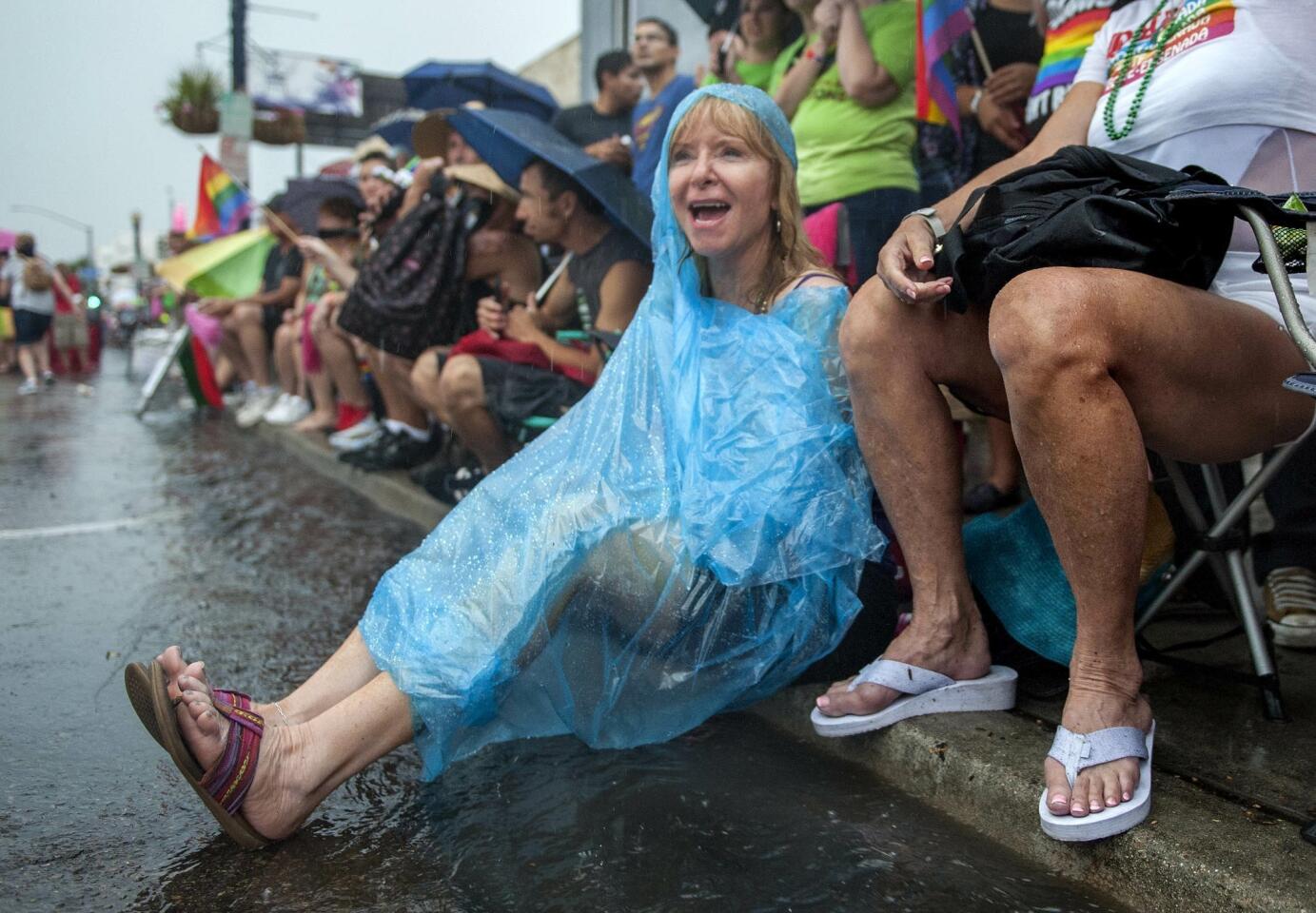 Jennifer Roth wears a poncho as she sits above the flowing storm drains watching the San Diego Pride Parade.