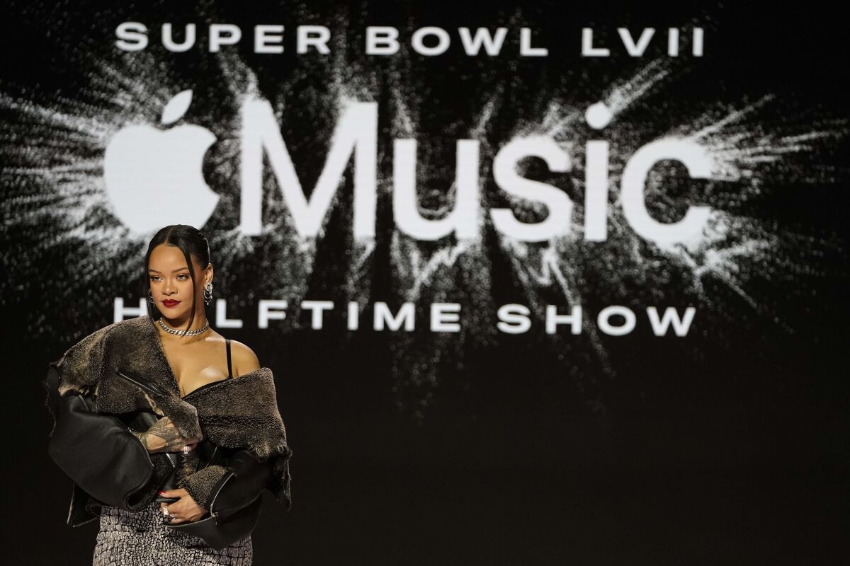 A woman with her jacket falling off one shoulder poses in front of a big logo