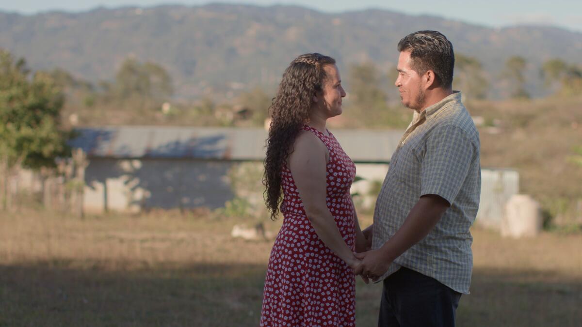 A woman and a man stand outside holding hands and looking at each other