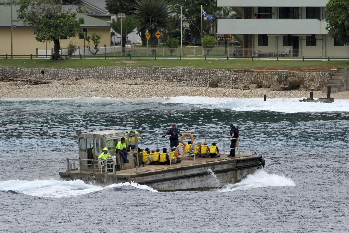 People wearing yellow life vests are seated on a barge approaching the shore