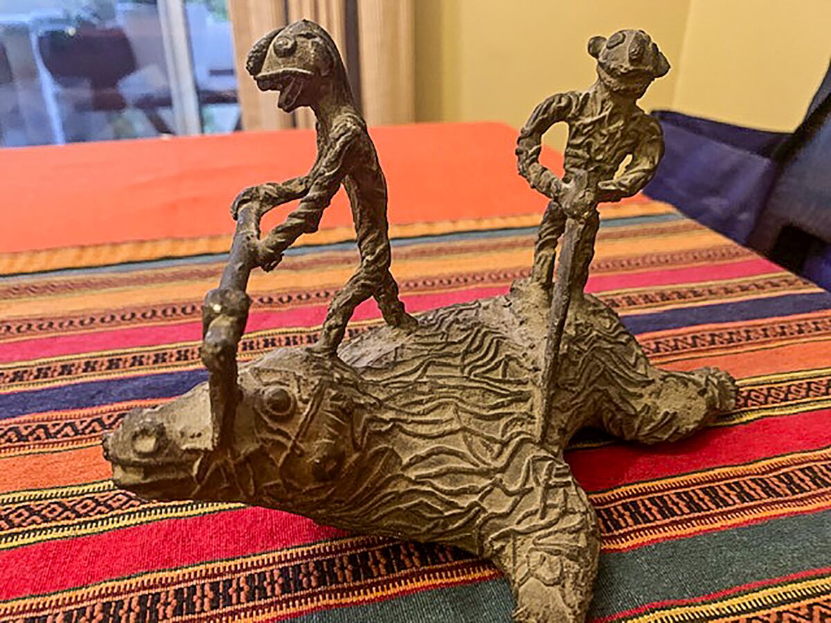 A statuette of a beast being butchered on a striped orange blanket in India. The buyer of this remembrance from India still doesn't understand its meaning.