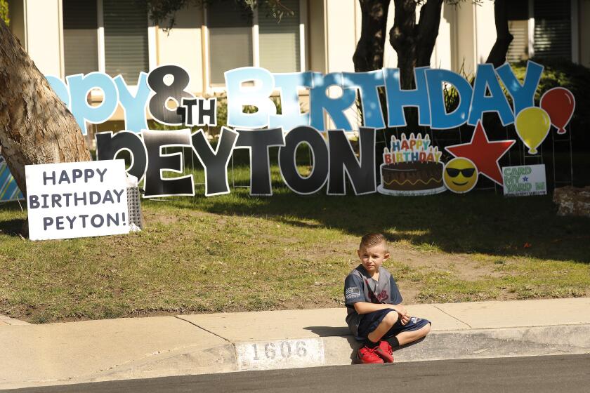 THOUSAND OAKS, CA - APRIL 16: Peyton Buss waits for cars full of fellow team members from his 2019 Conejo Valley Little League All Star Baseball Team to drive by his home in Thousand Oaks to celebrate his 8th birthday amid the coronavirus Covid-19 pandemic. Peyton's parents, Jill and Daniel Buss with the help of friends organized a "drive-by birthday party" with family and his best friends. Over 25 vehicles filled with cheering parents and children drove around his cul de sac in front of the Buss home several times bestowing Peyton with balloons, gifts, cards and placards. "This is the best birthday party I've ever had !" exclaimed Peyton. "People need social interaction," said his Mother Jill, "this is a new norm so we have to make due." Thousand Oaks on Thursday, April 16, 2020 in Thousand Oaks, CA. (Al Seib / Los Angeles Times)