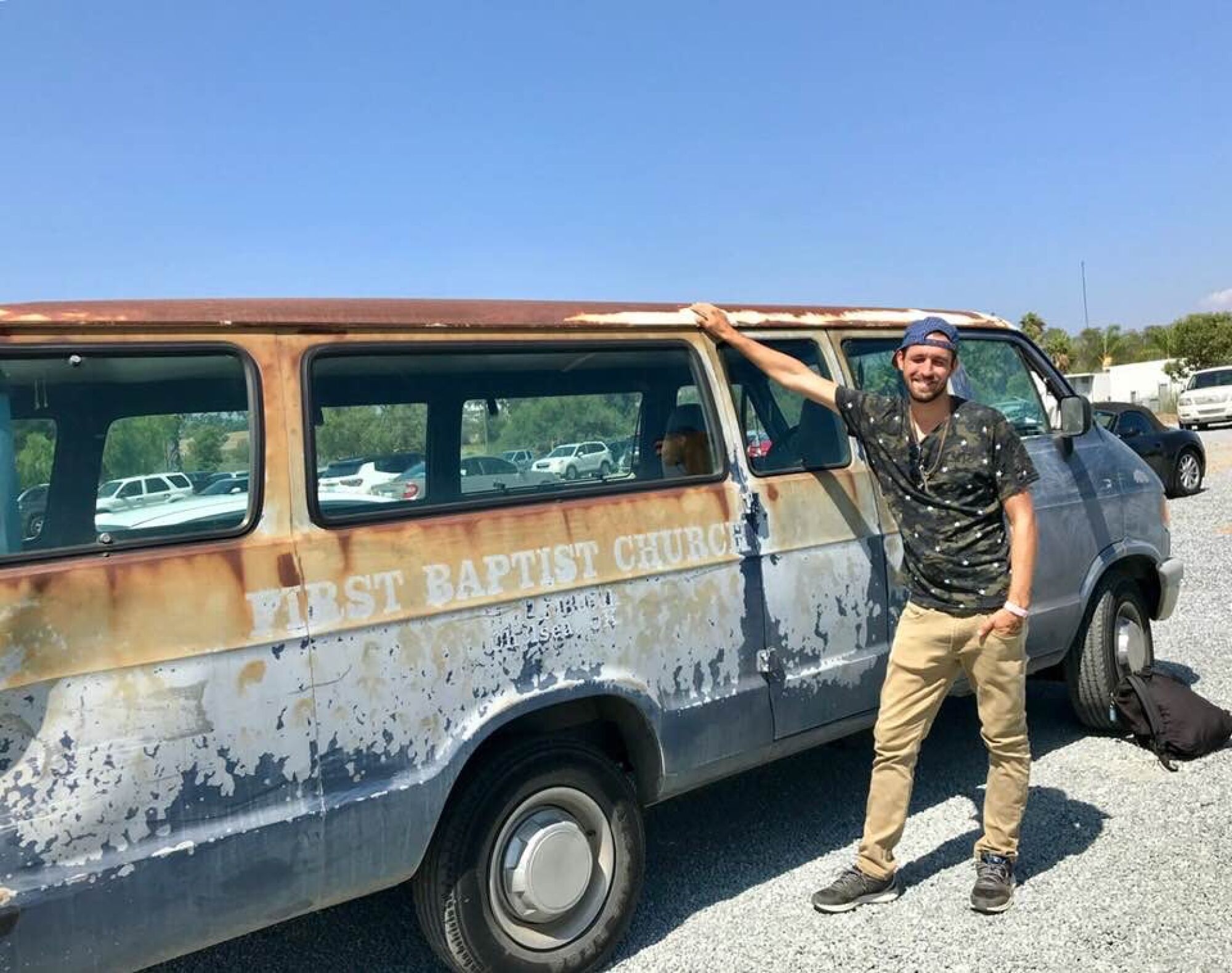 A photo of Luke Locatell next to a rusted First Baptist Church van in 2019. 