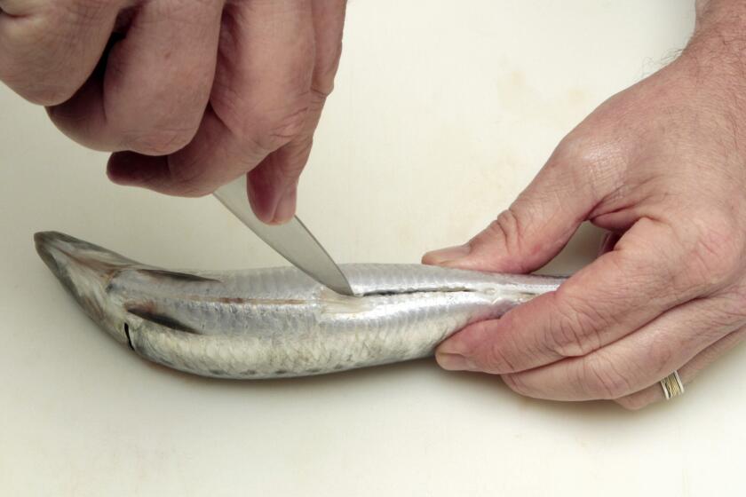 Begin by laying the fish on a board and making a small cut on the back, right behind the head and straight down through the backbone. Make another incision on the belly side just behind the front fins.
