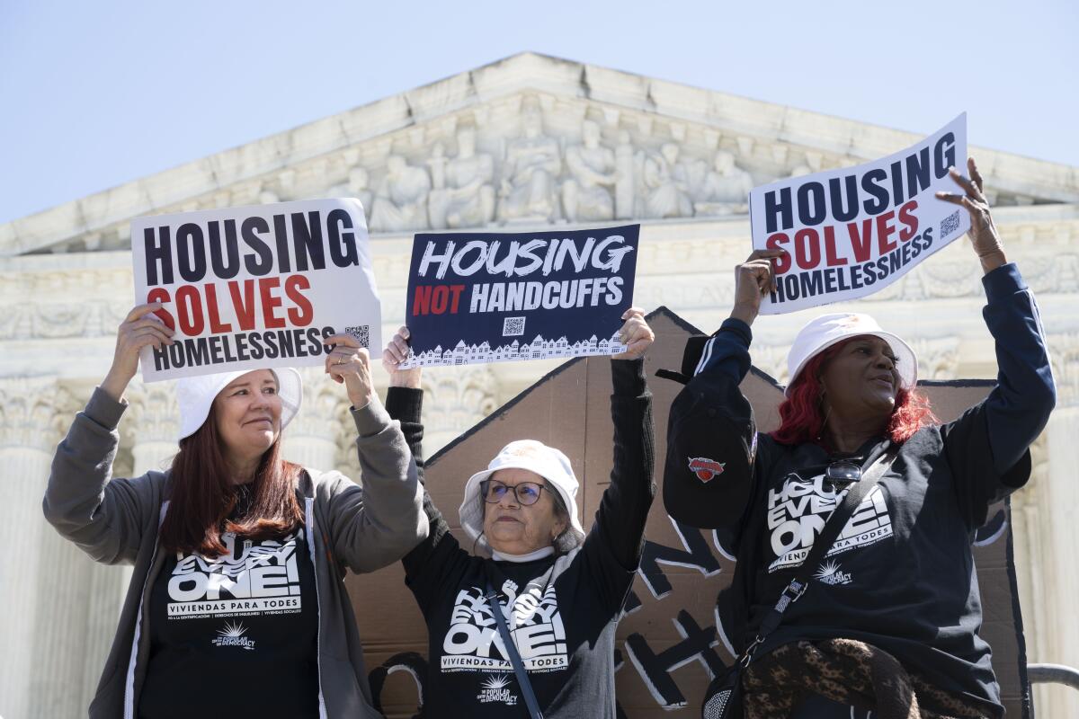 Three people hold up signs that say "Housing not handcuffs" and "Housing solved homelessness." 