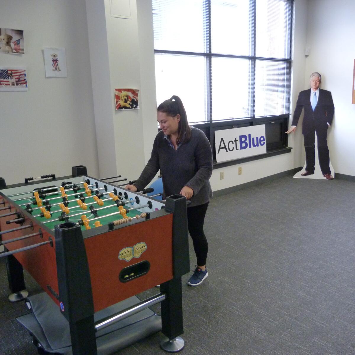 Marketing manager Hannah Brown hits the foosballl table in the game room at ActBlue's Somerville, Mass., headquarters. Behind her is a cardboard cutout of Bill Clinton.