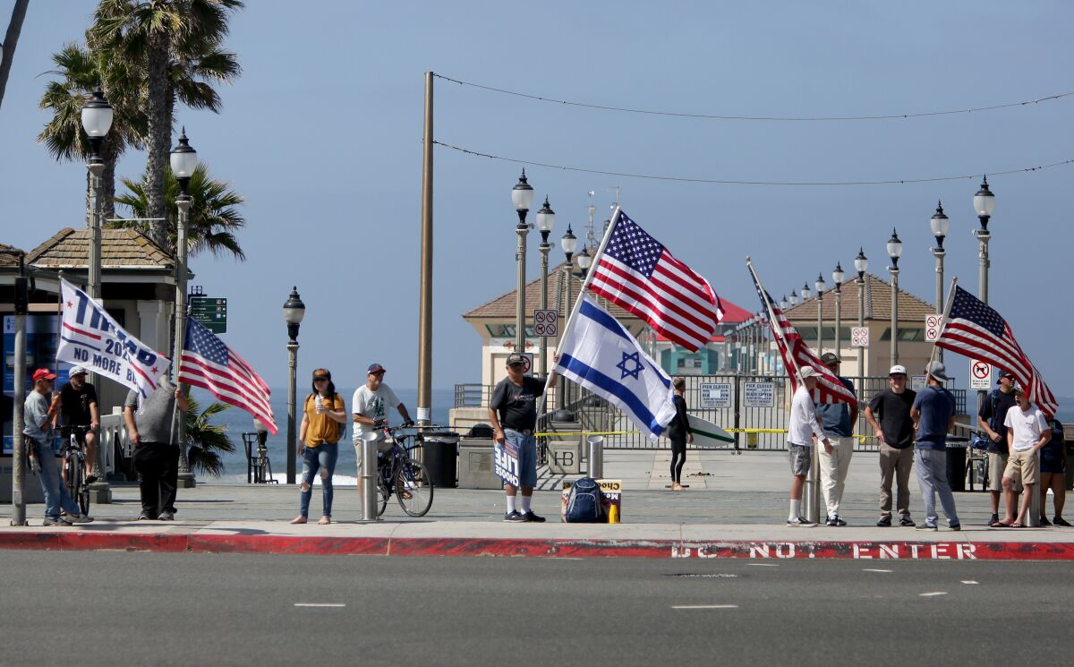 Some protesters hold flags and signs up at the entrance to the pier in Huntington Beach on Saturday.