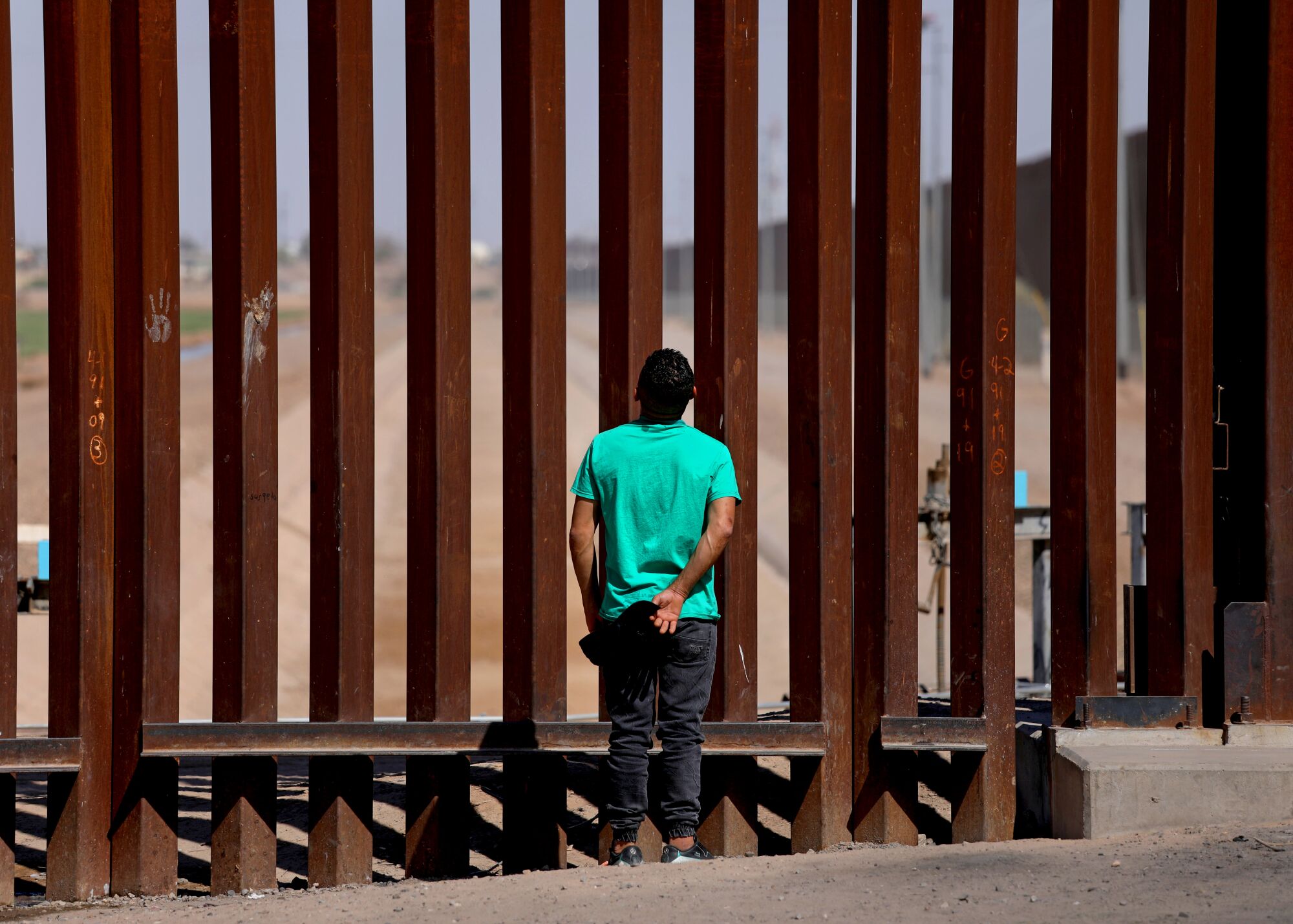 An person faces away while they look up at a tall fence made of thick metal posts