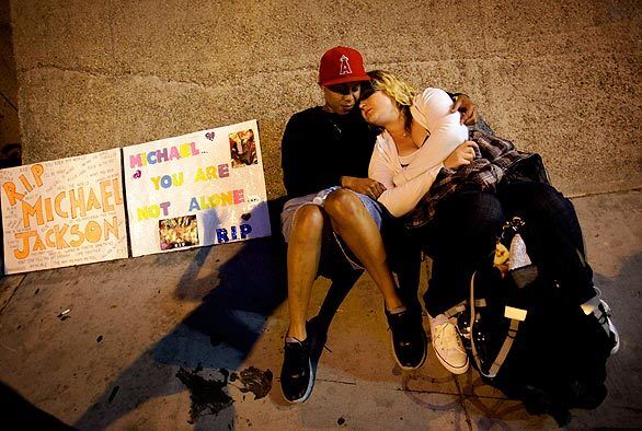 From left, Michelle Ushe and Cassandra Anderson from Orange County relax on Olympic Boulevard in the early morning hours as they wait for the Michael Jackson public memorial to start.