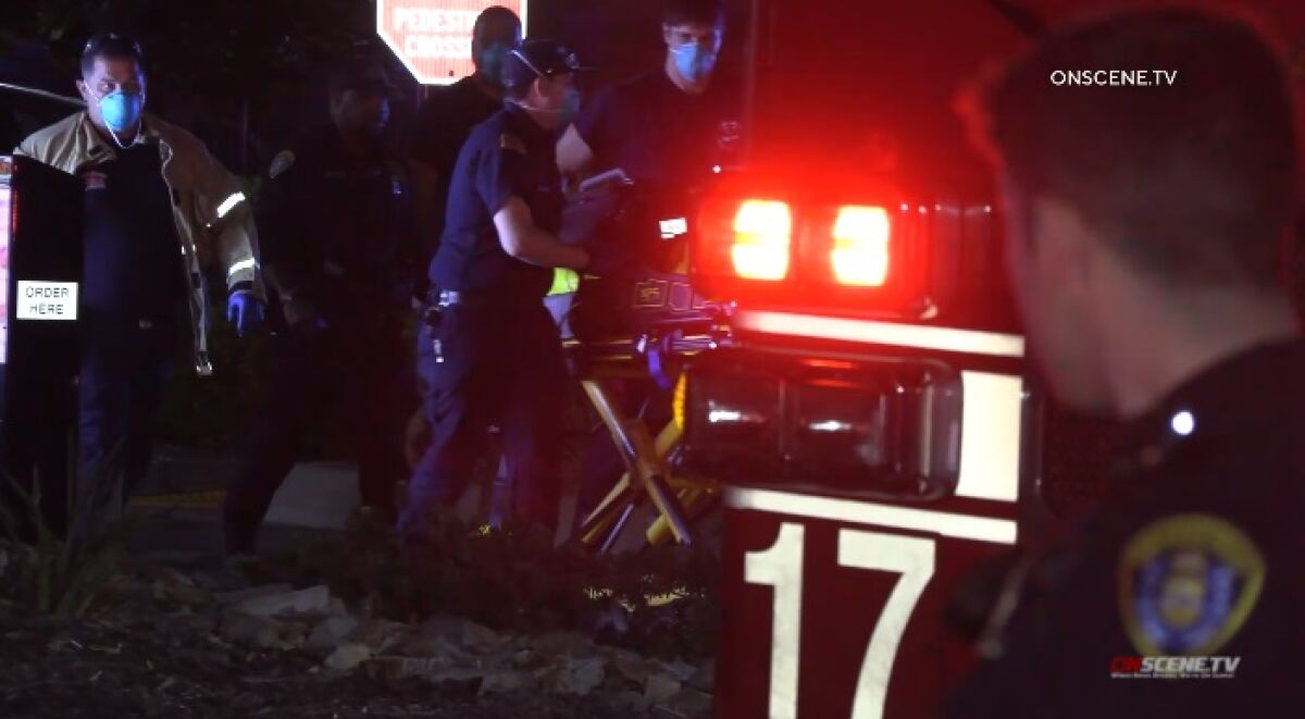A police officer watches as paramedics roll a gurney carrying a man who was shot by police Friday night in City Heights.
